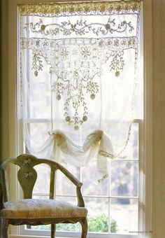 a chair sitting in front of a window next to a white curtain with bows on it