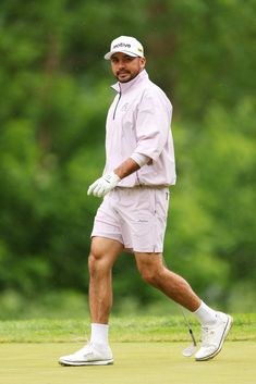 a man walking across a green covered golf course wearing white gloves and holding a club