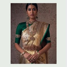 a woman in a green and gold sari with jewelry on her neck, standing next to a wall