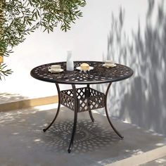 an outdoor table with two cups on it next to a potted plant and tree