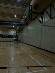 an indoor basketball court with hard wood flooring and white painted walls, lights are on