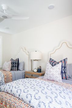 two beds in a bedroom next to each other with pillows on the bed and lamps