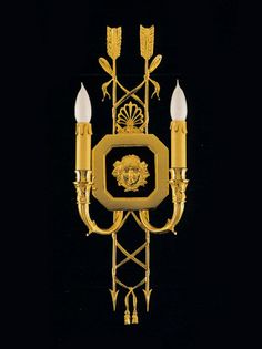 a wall mounted light with two candles on it's side and an ornate design