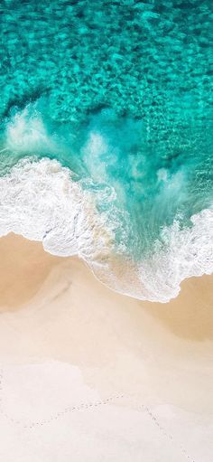 an aerial view of the ocean and beach with waves crashing in to shore, as seen from above