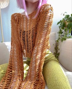 a woman with pink hair sitting on a couch wearing a knitted shawl over her shoulders