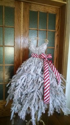 a dress made out of tinsel is sitting in front of a door with a red and white ribbon on it