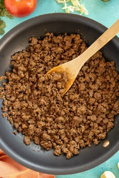 a wooden spoon in a skillet filled with ground beef and tomatoes on the side