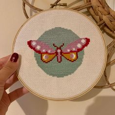 a hand is holding up a cross - stitch butterfly in front of a wall hanging