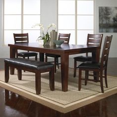 a dining room table with chairs and a vase on the rug in front of it