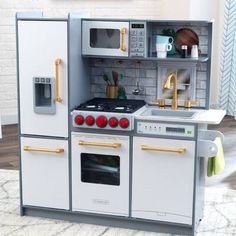 a toy kitchen with white appliances and gold handles on the stove, oven, microwave and sink