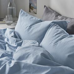 a bed with blue sheets and pillows next to a vase filled with flowers on a table