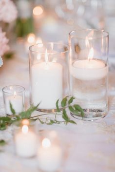 candles are lit on a table with flowers and greenery