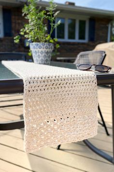 a crocheted table runner on a patio with sunglasses and potted plant in the background