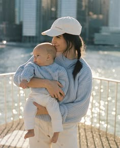 a woman holding a baby in her arms while standing on a pier near the water