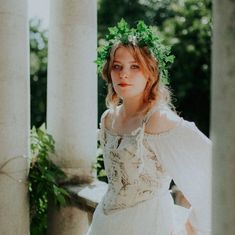 a woman in a white dress standing next to columns and wearing a wreath on her head