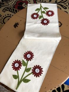 an embroidered table runner with red flowers on it and two white buttons in the middle