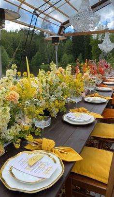 a long table set with yellow and white plates, napkins and flowers in vases