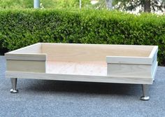 a wooden box sitting on top of a cement ground next to some bushes and shrubbery