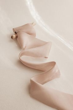 two pieces of pink satin ribbon laying on top of a white bed sheet with a wooden pin