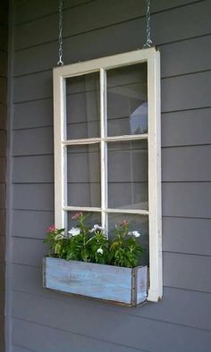 an old window is hung on the side of a gray house with flowers in it