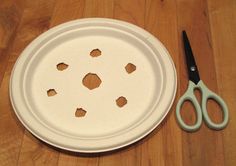 a pair of scissors sitting next to a paper plate with holes cut out on it