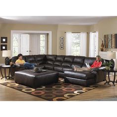 two people sitting on a couch in a living room with a large brown sectional sofa