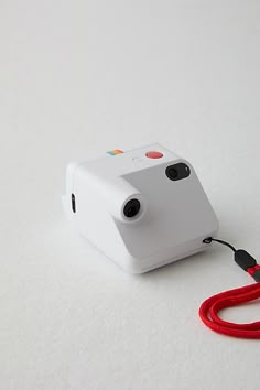 a camera with a red cord attached to it on a white surface and a black object in the background