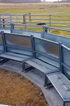 three metal benches sitting next to each other near a fenced in area with cattle