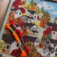 a cross stitch pattern with two crochet hooks and an orange tassel on it