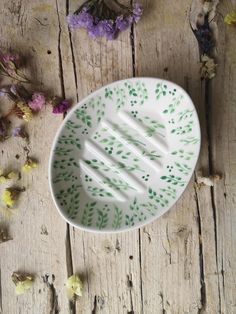 a white plate with green leaves on it sitting on a wooden table next to dried flowers