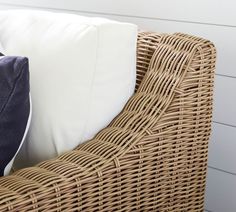 a wicker chair with two pillows on it and a white wall in the background