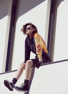 a woman sitting on top of a metal rail with her legs crossed and wearing black sneakers