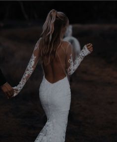 a woman in a white wedding dress holding the hand of a man wearing a black suit