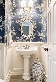 a white sink sitting under a bathroom mirror next to a blue and white wallpaper