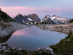 a small lake surrounded by mountains under a pink sky