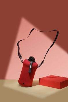 a red bag sitting on top of a table next to a red box with a black strap