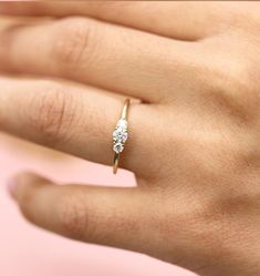 a woman's hand with a diamond ring on top of her finger, against a pink background