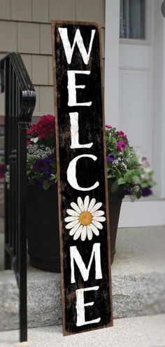 a wooden welcome sign sitting on the side of a building next to a flower pot