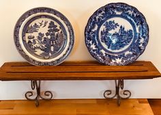 two blue and white plates sitting on top of a wooden shelf