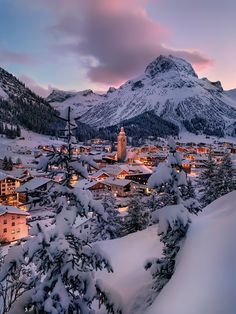 the town is surrounded by snow covered trees and mountain range in the background at dusk