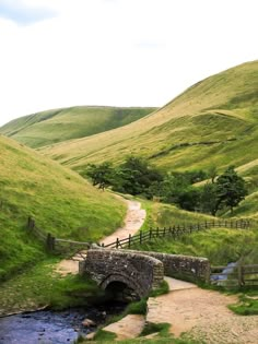 a stone bridge over a stream in the middle of a lush green valley