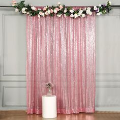 a pink curtain with flowers on it next to a white vase