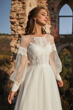 a woman standing in front of a window wearing a wedding dress with long sleeves and sheer lace