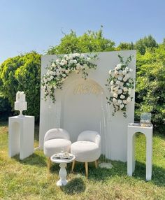 an outdoor ceremony setup with white chairs and flowers on the arch, surrounded by greenery