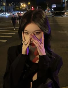 a woman covers her face with her hands as she stands in the street at night