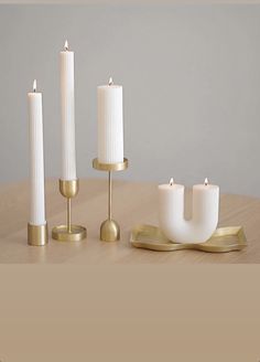 three white candles sitting on top of a wooden table next to two gold candle holders