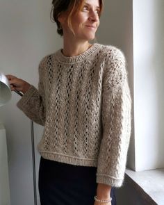 a woman standing in front of a window wearing a knitted sweater and holding a ladle