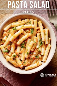 pasta salad in a white bowl on top of a wooden table next to a fork