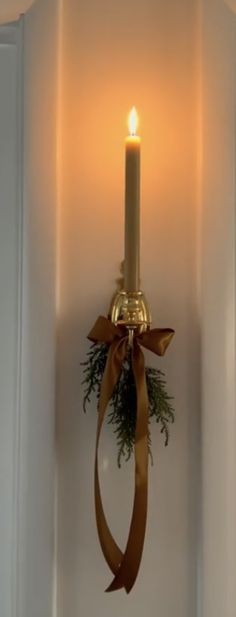 a lit candle with a ribbon hanging from it's side on a wall next to a window