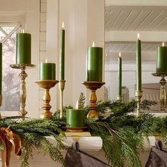 green candles are sitting on a mantle with evergreen garland and stockings hanging from the mantel